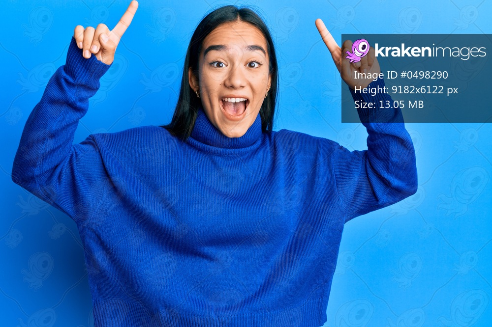 Young asian woman wearing casual winter sweater smiling amazed and surprised and pointing up with fingers and raised arms. 