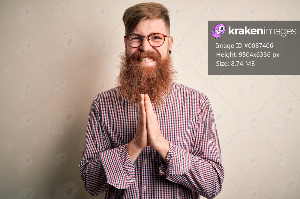 Handsome Irish redhead business man with beard wearing glasses over isolated background praying with hands together asking for forgiveness smiling confident.