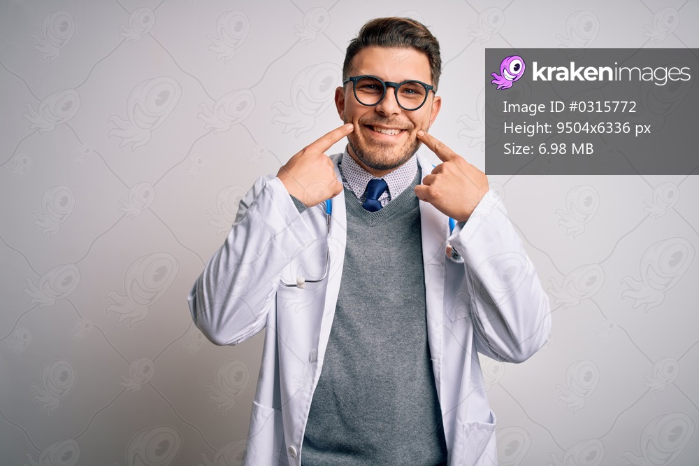 Young doctor man with blue eyes wearing medical coat and stethoscope over isolated background Smiling with open mouth, fingers pointing and forcing cheerful smile