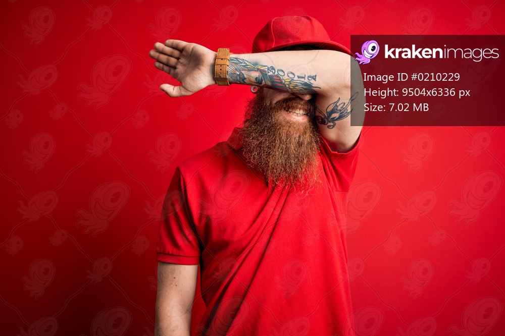Young handsome delivery man wearing glasses and red cap over isolated background covering eyes with arm smiling cheerful and funny. Blind concept.