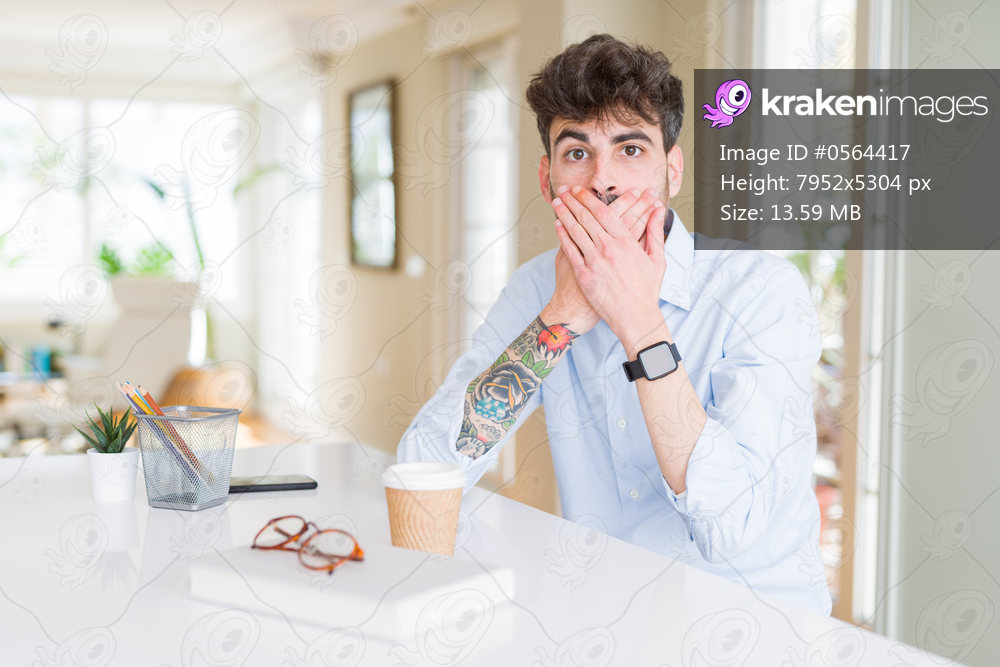 Young business man working shocked covering mouth with hands for mistake. Secret concept.