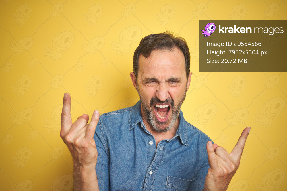 Handsome middle age senior man with grey hair over isolated yellow background shouting with crazy expression doing rock symbol with hands up. Music star. Heavy concept.