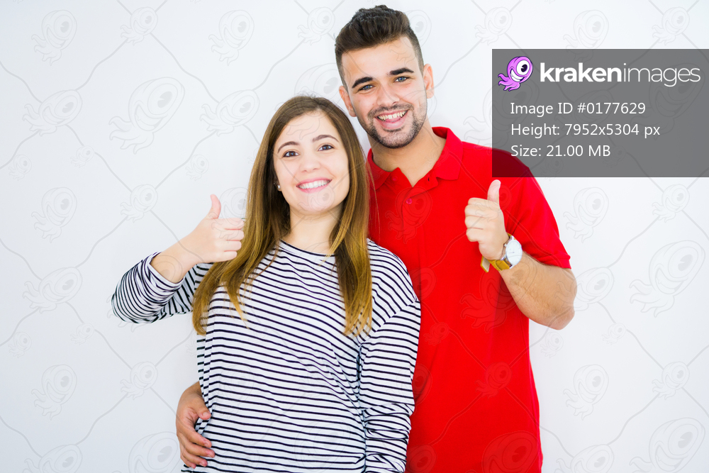 Young beautiful couple together over white isolated background doing happy thumbs up gesture with hand. Approving expression looking at the camera with showing success.