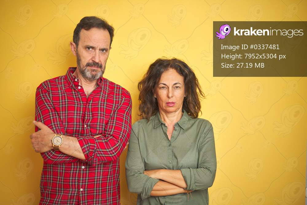 Beautiful middle age couple over isolated yellow background skeptic and nervous, disapproving expression on face with crossed arms. Negative person.