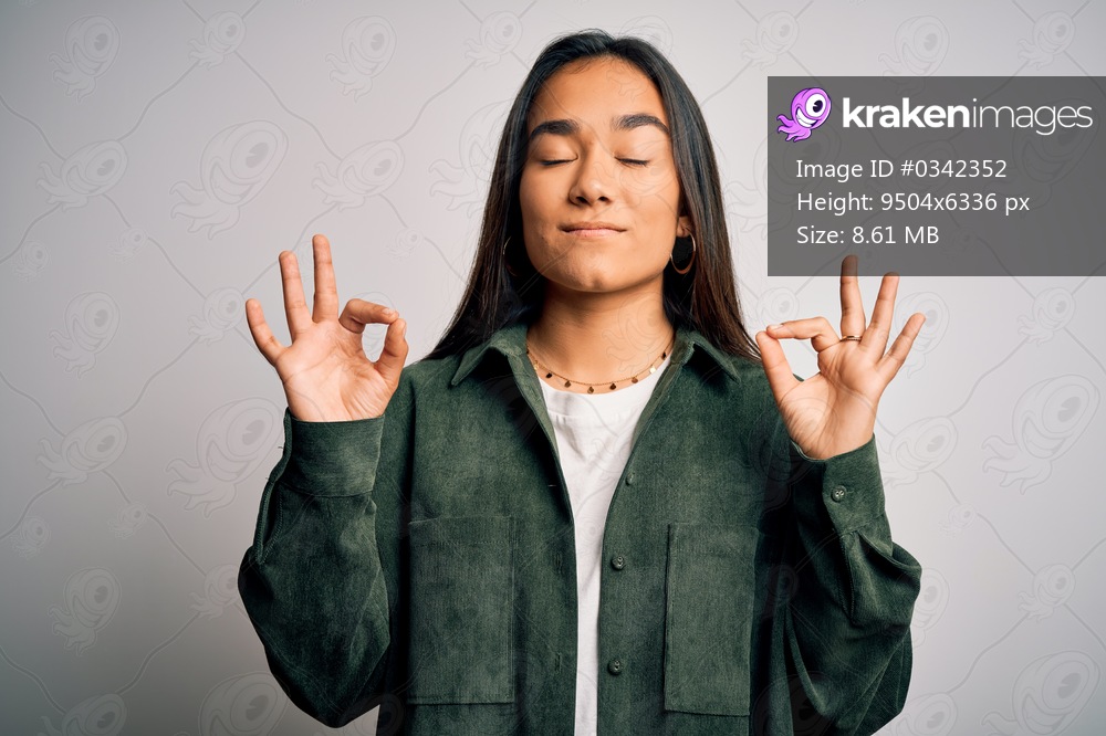 Young beautiful asian woman wearing casual shirt standing over isolated white background relax and smiling with eyes closed doing meditation gesture with fingers. Yoga concept.