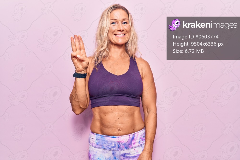 Middle age caucasian blonde woman wearing sportswear over pink background showing and pointing up with fingers number three while smiling confident and happy. 