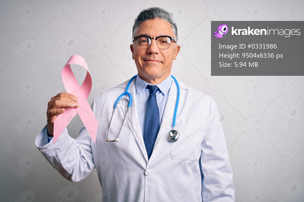 Middle age handsome grey-haired doctor man holding pink cancer ribbon with a happy face standing and smiling with a confident smile showing teeth