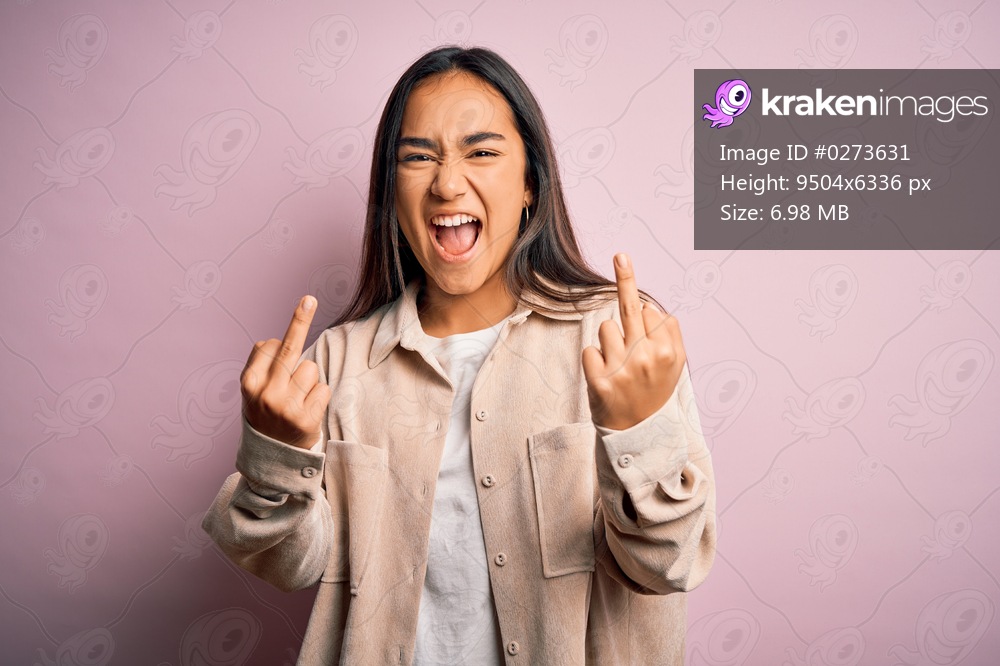 Young beautiful asian woman wearing casual shirt standing over pink background Showing middle finger doing fuck you bad expression, provocation and rude attitude. Screaming excited