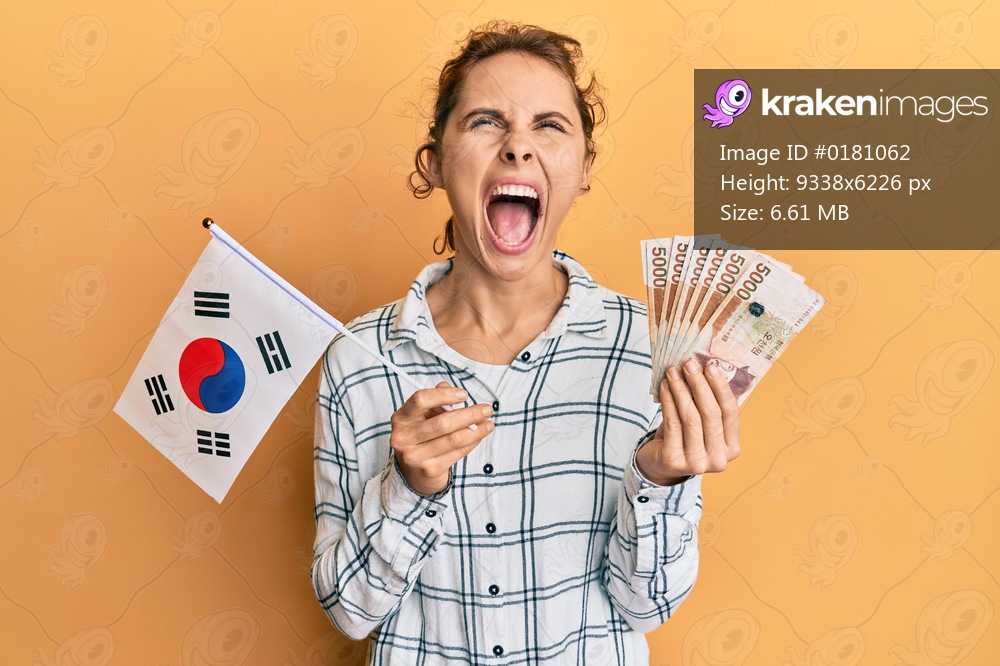 Young brunette woman holding south korean won banknotes angry and mad screaming frustrated and furious, shouting with anger looking up. 