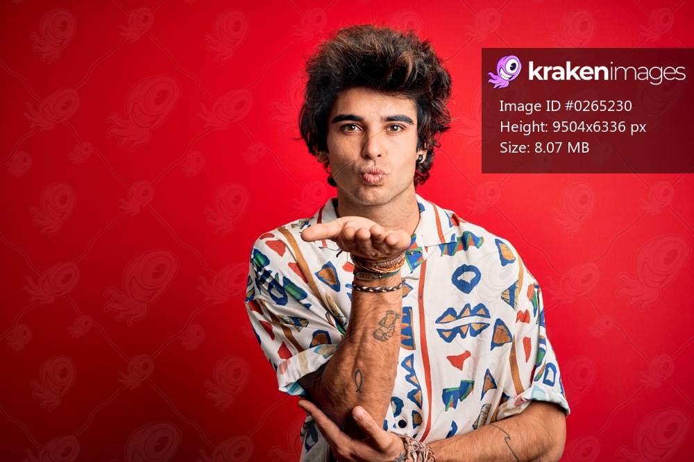 Young handsome man on vacation wearing summer shirt over isolated red background looking at the camera blowing a kiss with hand on air being lovely and sexy. Love expression.