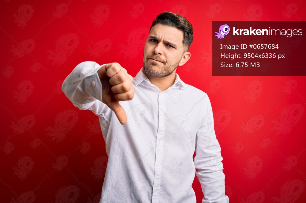 Young business man with blue eyes wearing elegant shirt standing over red isolated background looking unhappy and angry showing rejection and negative with thumbs down gesture. Bad expression.