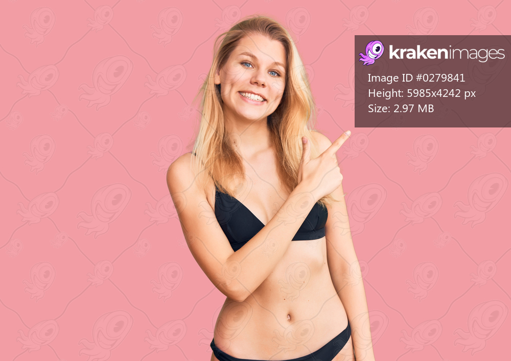 Young beautiful blonde woman wearing bikini cheerful with a smile on face pointing with hand and finger up to the side with happy and natural expression 