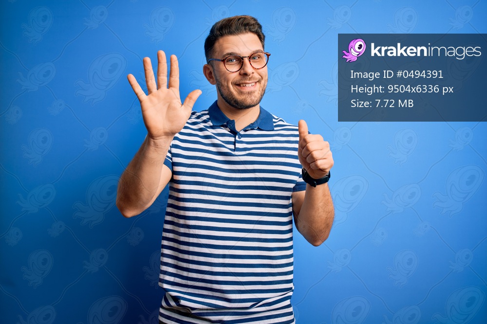 Young man with blue eyes wearing glasses and casual striped t-shirt over blue background showing and pointing up with fingers number six while smiling confident and happy.