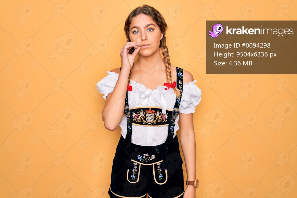 Young beautiful blonde german woman with blue eyes wearing traditional octoberfest dress mouth and lips shut as zip with fingers. Secret and silent, taboo talking