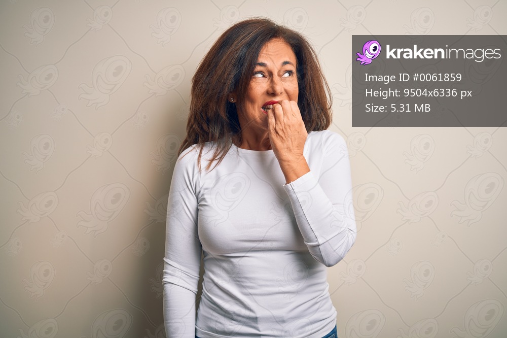 Middle age beautiful woman wearing casual t-shirt standing over isolated white background looking stressed and nervous with hands on mouth biting nails. Anxiety problem.
