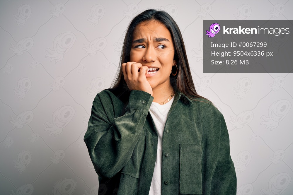 Young beautiful asian woman wearing casual shirt standing over isolated white background looking stressed and nervous with hands on mouth biting nails. Anxiety problem.