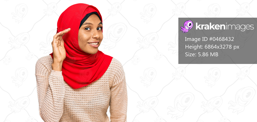 Young african american woman wearing traditional islamic hijab scarf smiling with hand over ear listening an hearing to rumor or gossip. deafness concept. 