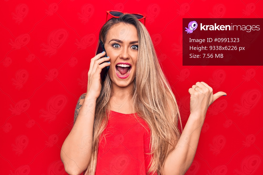 Beautiful blonde woman having conversation talking on the smartphone over red background pointing thumb up to the side smiling happy with open mouth