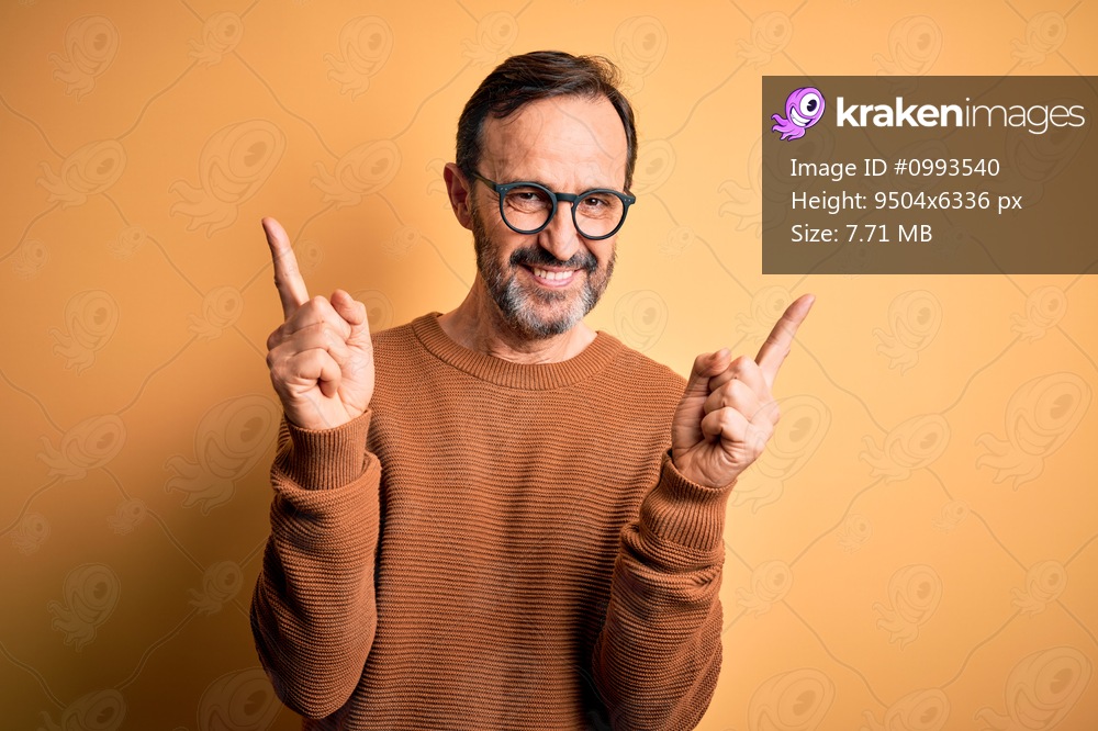 Middle age hoary man wearing brown sweater and glasses over isolated yellow background smiling confident pointing with fingers to different directions. Copy space for advertisement