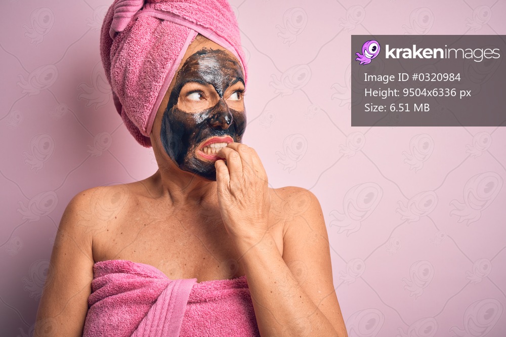 Middle age brunette woman wearing beauty black face mask over isolated pink background looking stressed and nervous with hands on mouth biting nails. Anxiety problem.