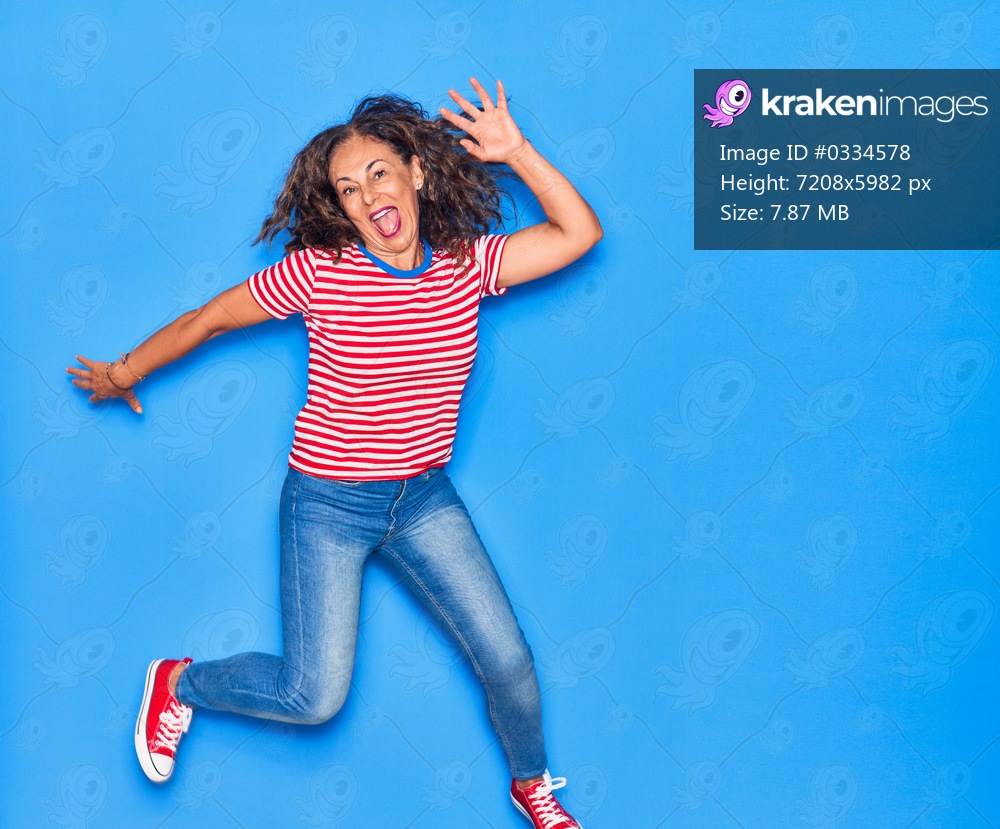 Middle age beautiful hispanic woman wearing casual clothes smiling happy. Jumping with smile on face over isolated blue background