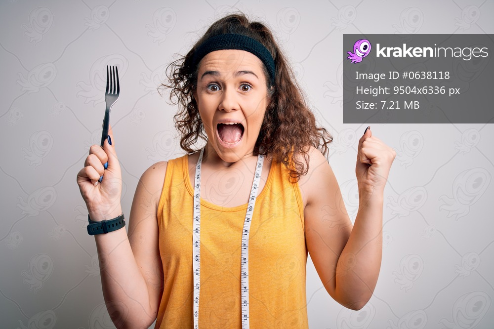 Young beautiful woman with curly hair doing diet holding fork and tape measure screaming proud and celebrating victory and success very excited, cheering emotion