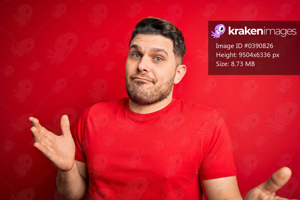 Young man with blue eyes wearing casual t-shirt over red isolated background clueless and confused expression with arms and hands raised. Doubt concept.