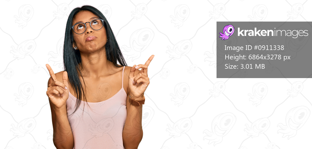 Young african american woman wearing casual clothes and glasses pointing up looking sad and upset, indicating direction with fingers, unhappy and depressed. 