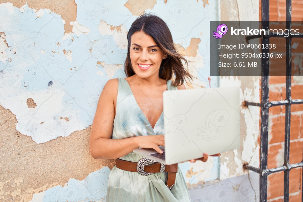 Beautiful young woman wearing fashionable clothes walking down the street and working using computer laptop