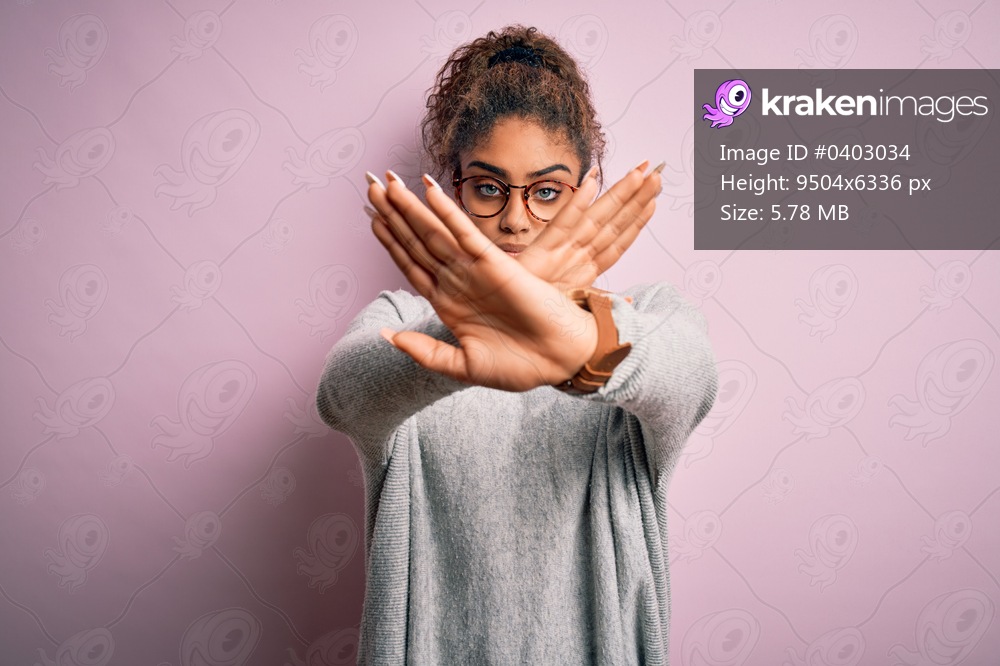 Young beautiful african american girl wearing sweater and glasses over pink background Rejection expression crossing arms and palms doing negative sign, angry face