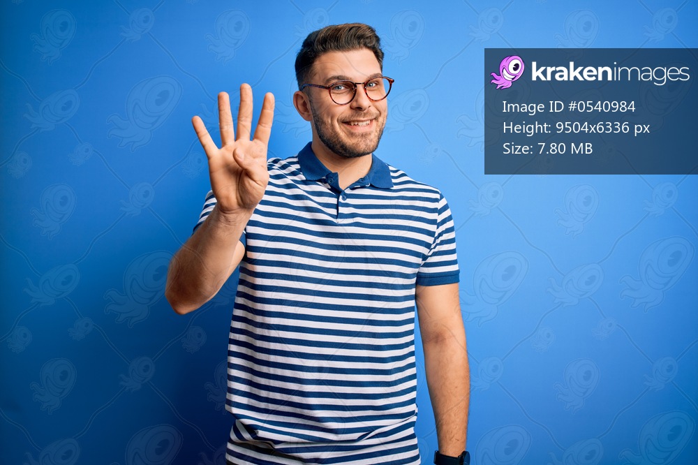 Young man with blue eyes wearing glasses and casual striped t-shirt over blue background showing and pointing up with fingers number four while smiling confident and happy.
