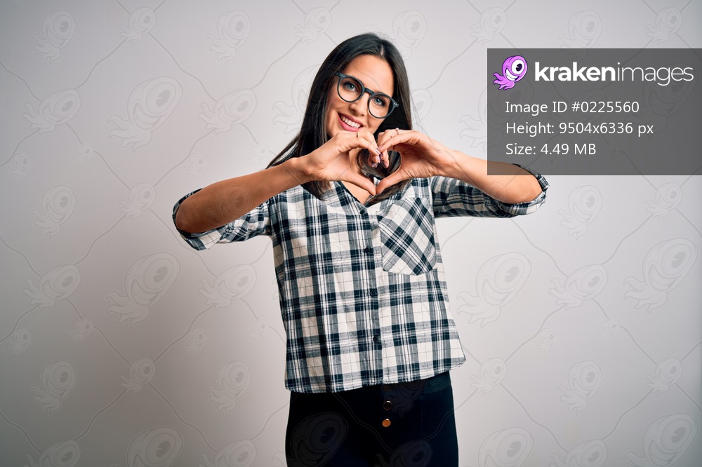 Young brunette woman with blue eyes wearing casual shirt and glasses over white background smiling in love doing heart symbol shape with hands. Romantic concept.
