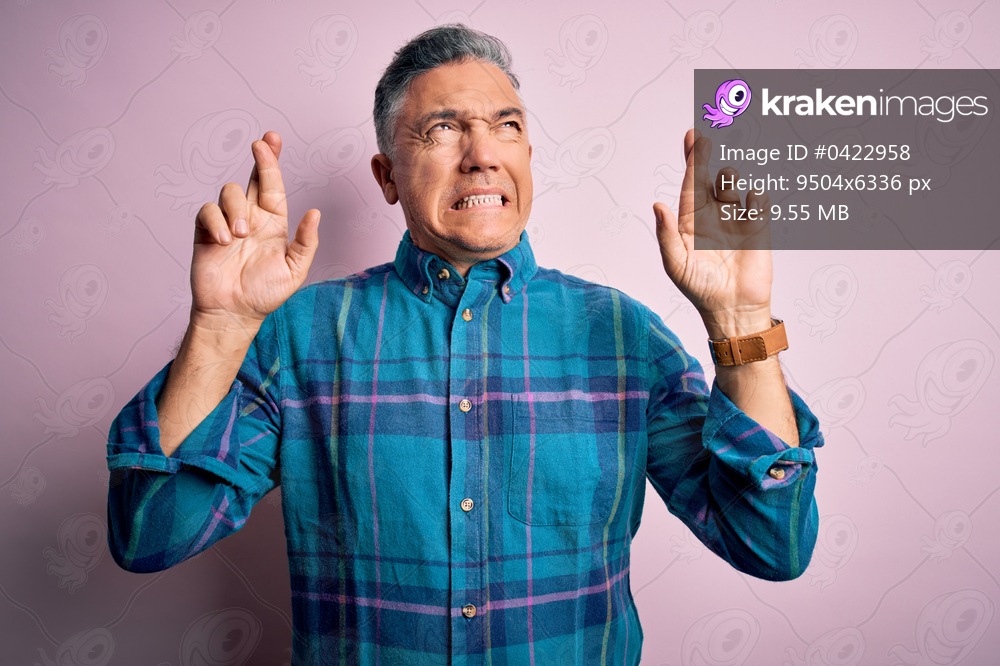 Middle age handsome grey-haired man wearing casual shirt over isolated pink background gesturing finger crossed smiling with hope and eyes closed. Luck and superstitious concept.
