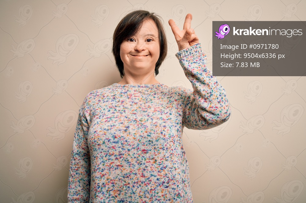 Young down syndrome woman standing over isolated background smiling with happy face winking at the camera doing victory sign. Number two.