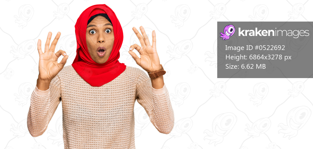 Young african american woman wearing traditional islamic hijab scarf looking surprised and shocked doing ok approval symbol with fingers. crazy expression 