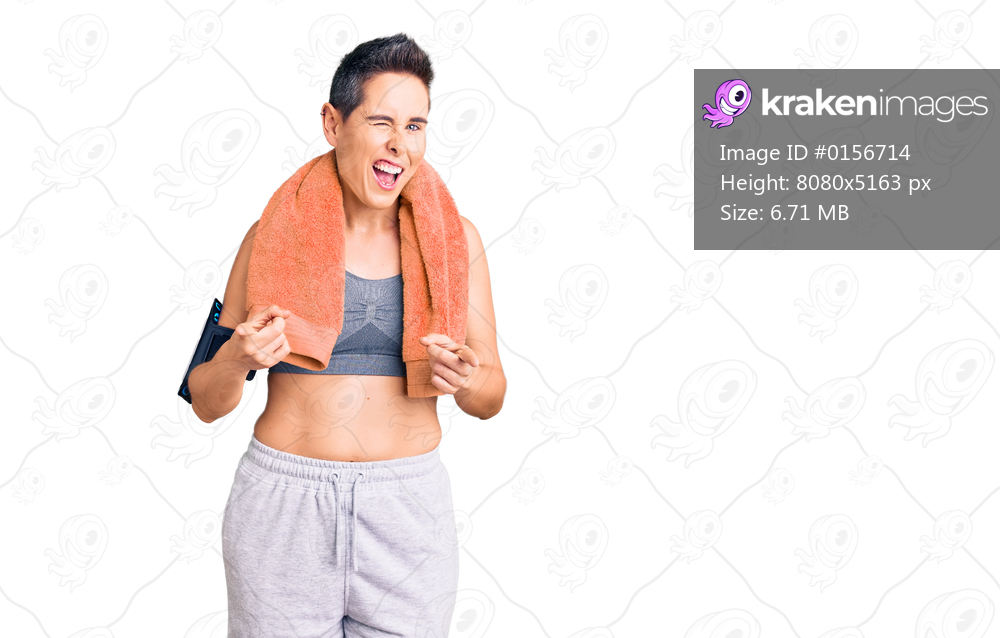 Young woman with short hair wearing sportswear and towel using smartphone pointing fingers to camera with happy and funny face. good energy and vibes. 