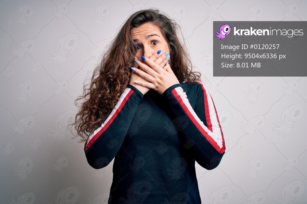 Young beautiful woman with curly hair wearing casual sweater over isolated white background shocked covering mouth with hands for mistake. Secret concept.