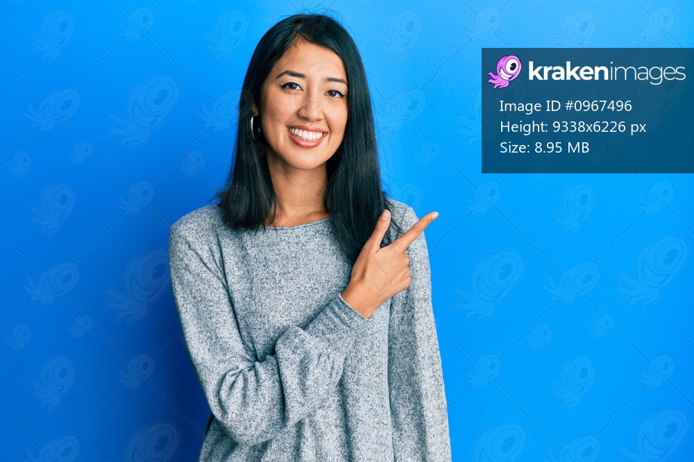 Beautiful asian young woman wearing casual clothes smiling cheerful pointing with hand and finger up to the side 