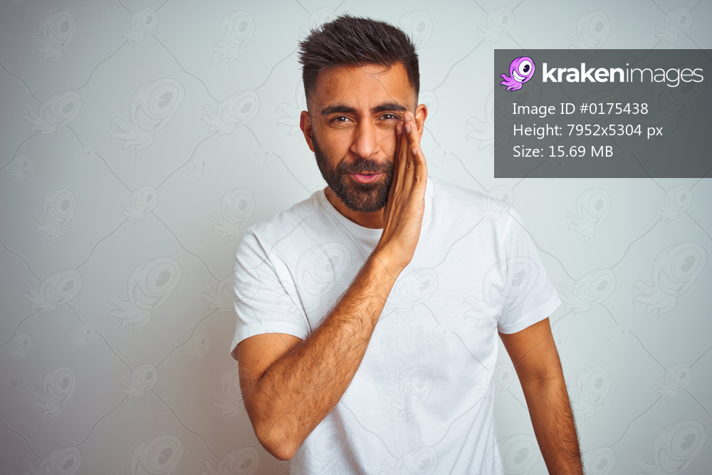 Young indian man wearing t-shirt standing over isolated white background hand on mouth telling secret rumor, whispering malicious talk conversation