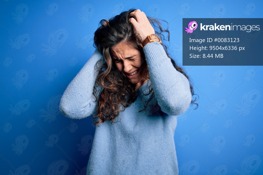 Young beautiful woman with curly hair wearing blue casual sweater over isolated background suffering from headache desperate and stressed because pain and migraine. Hands on head.