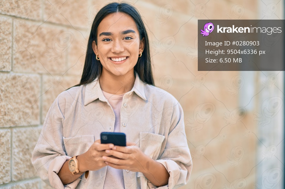 Young latin girl smiling happy using smartphone at the city.