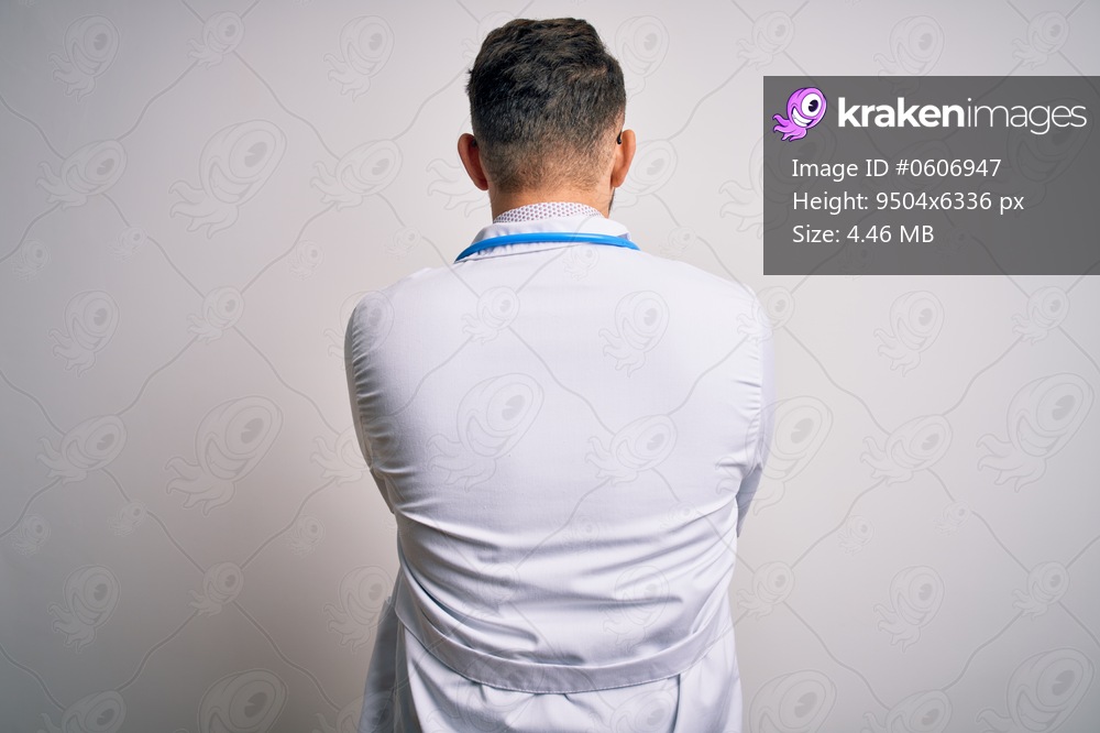 Young doctor man with blue eyes wearing medical coat and stethoscope over isolated background standing backwards looking away with crossed arms