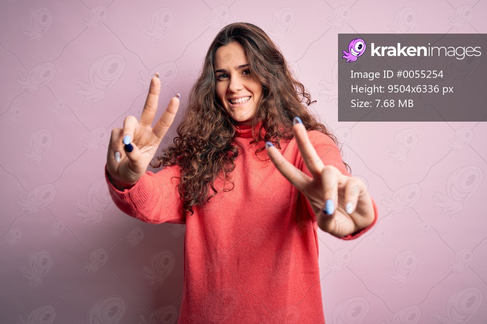Young beautiful woman with curly hair wearing turtleneck sweater over pink background smiling looking to the camera showing fingers doing victory sign. Number two.