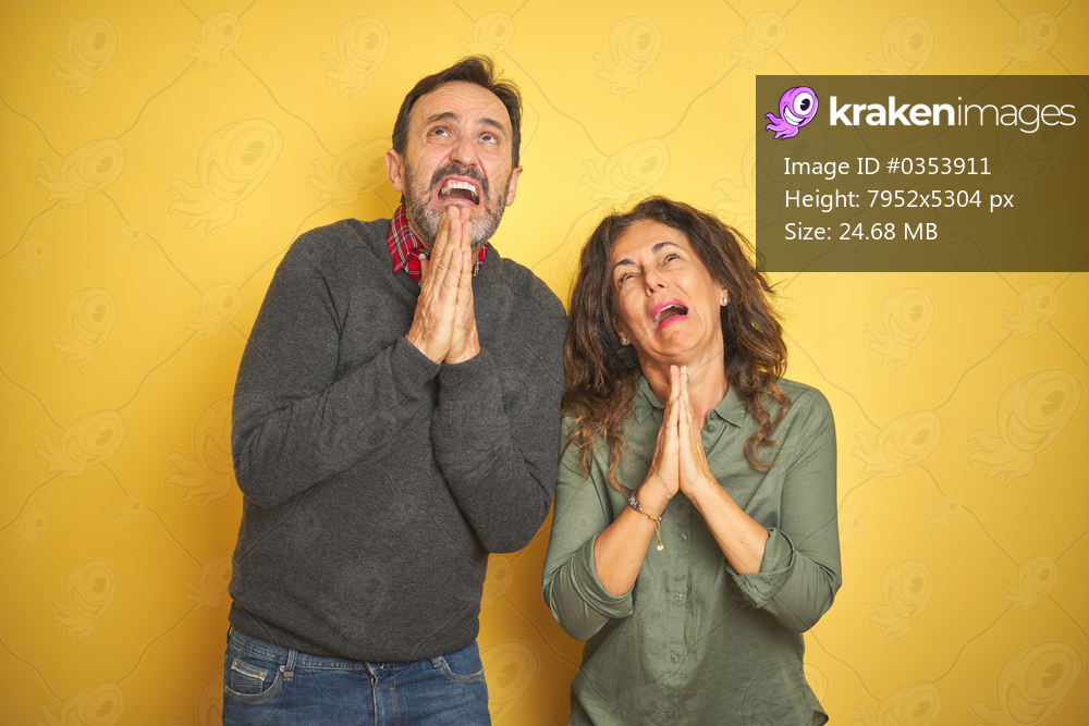 Beautiful middle age couple over isolated yellow background begging and praying with hands together with hope expression on face very emotional and worried. Asking for forgiveness. Religion concept.