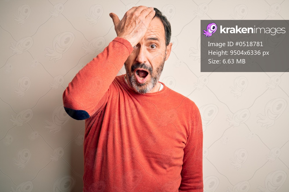 Middle age hoary man wearing casual orange sweater standing over isolated white background surprised with hand on head for mistake, remember error. Forgot, bad memory concept.
