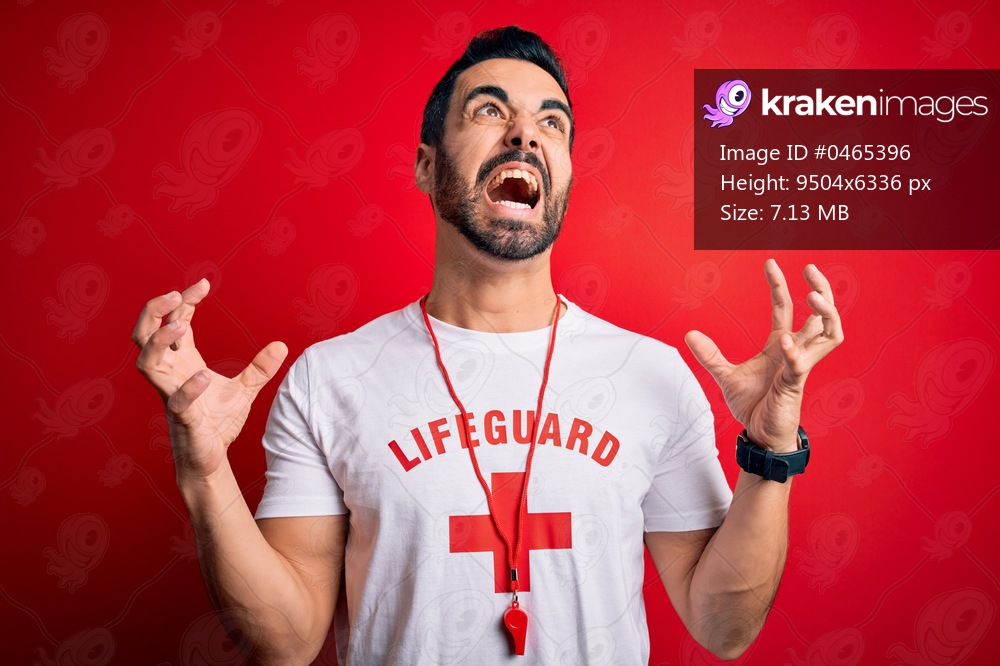 Young handsome lifeguard man with beard wearing whistle over isolated red background crazy and mad shouting and yelling with aggressive expression and arms raised. Frustration concept.