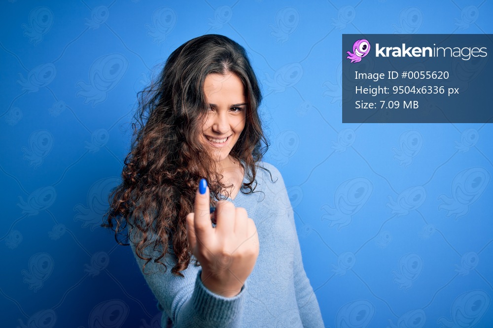 Young beautiful woman with curly hair wearing blue casual sweater over isolated background Beckoning come here gesture with hand inviting welcoming happy and smiling