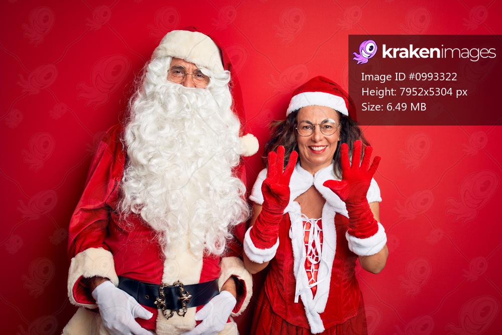Middle age couple wearing Santa costume and glasses over isolated red background showing and pointing up with fingers number eight while smiling confident and happy.