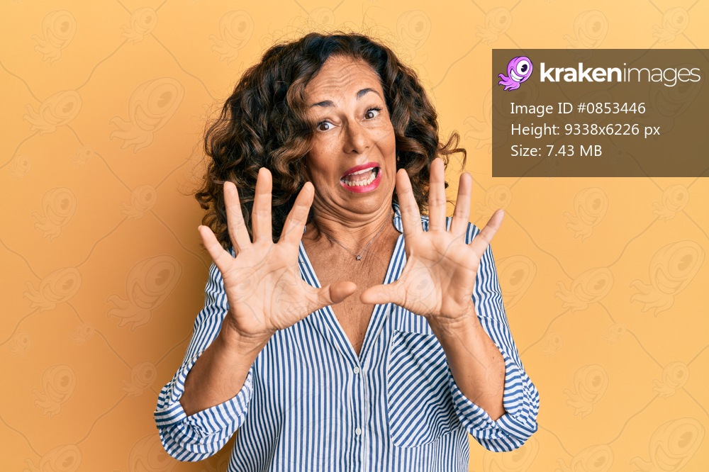 Middle age hispanic woman wearing casual clothes afraid and terrified with fear expression stop gesture with hands, shouting in shock. panic concept. 