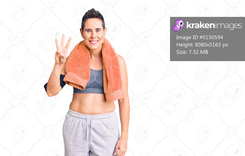 Young woman with short hair wearing sportswear and towel using smartphone showing and pointing up with fingers number three while smiling confident and happy. 